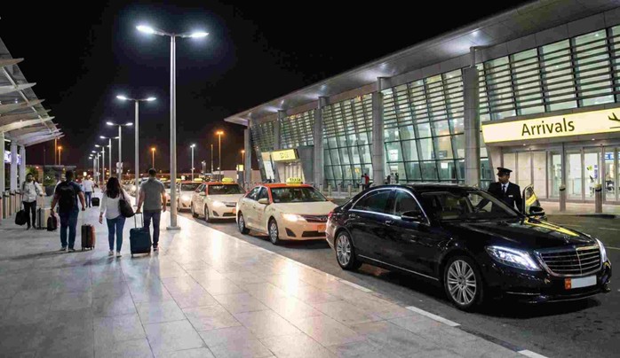 Taxis and a luxury private car waiting at the airport arrivals terminal during the evening, ready to transport passengers for an Abu Dhabi Layover Tour at Night.
