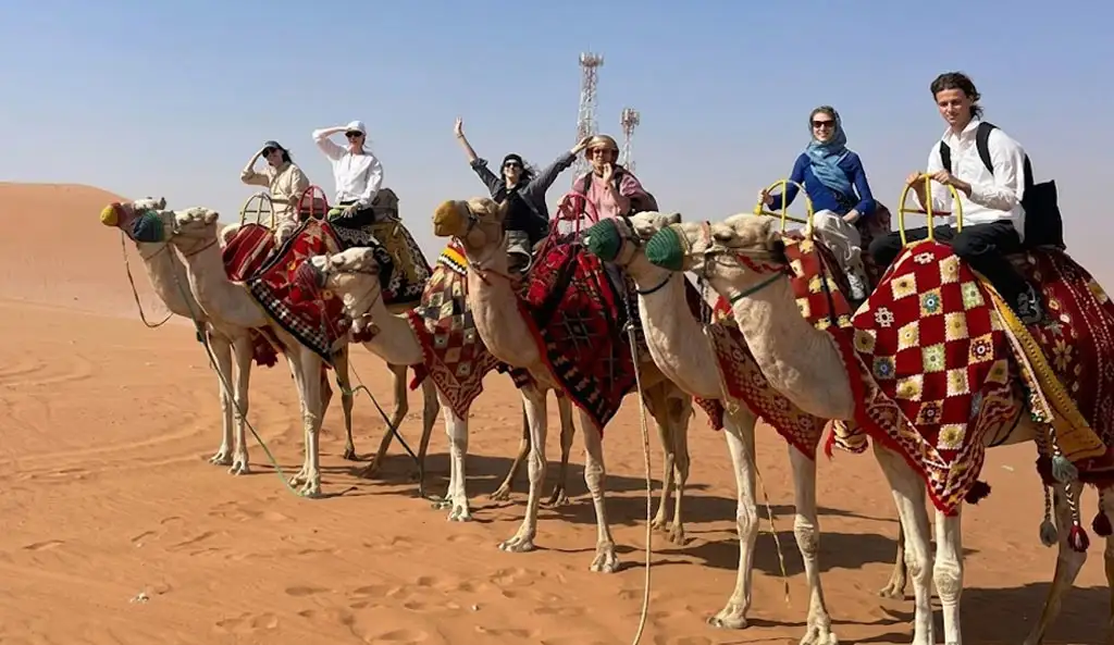 Happy group of tourists riding decorated camels in Riyadh Desert Safari, Saudi Arabia