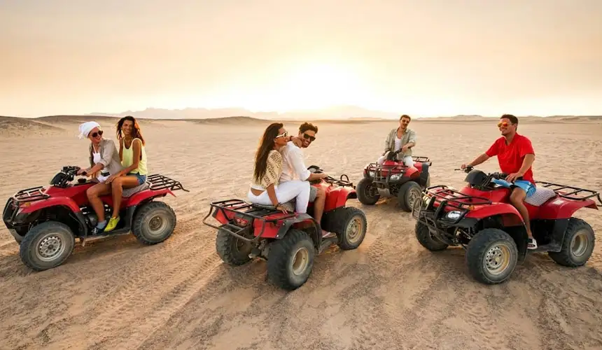Group of friends enjoying a magical sunset quad bike tour in Abu Dhabi desert on red ATVs. Beautiful golden hour desert experience with stunning sand dunes in the background.